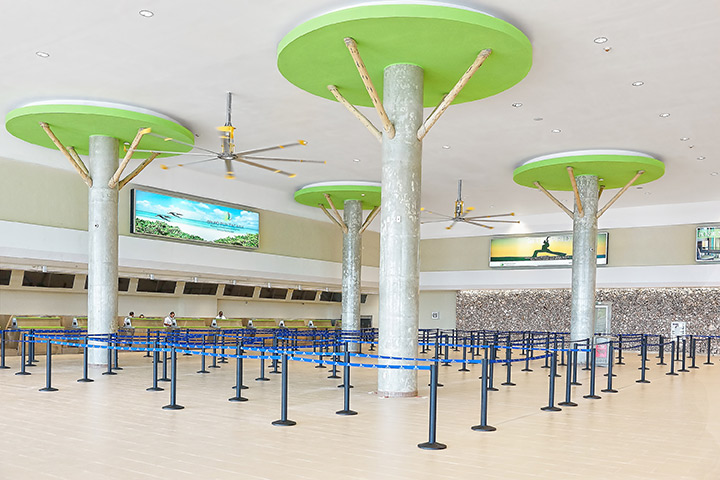 Punta Cana Airport installed a Delta Cooling energy efficient cooling tower system. There are big columns that are beige with a circular green top that makes them look like trees. There are poles that have lanes marked out with blue posts.  